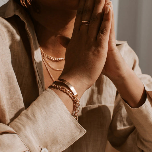 Close-up of person wearing layered gold necklaces, gold bracelets, and a gold ring on clasped hands